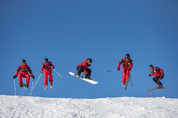 Skilehrer und Snowboardlehrer der Skischule Klosters springen auf der Piste